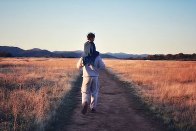 Rear view of man carrying son on shoulders while walking on land