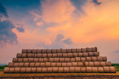 Stack of bales of hay on field against sky during sunset