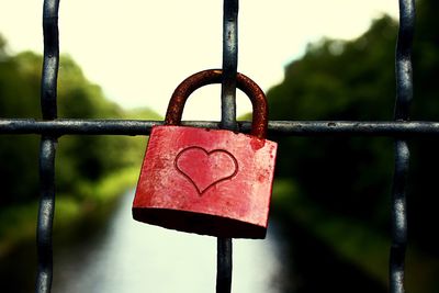 Close-up of red love padlock hanging on fence by canal