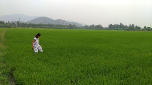 Mid adult woman standing on grassy field against sky