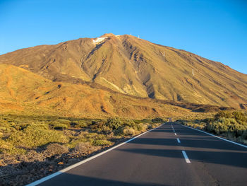 Road by mountain against clear blue sky