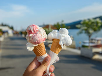 Personal perspective of hand holding two ice cream in cones on promenade by sea