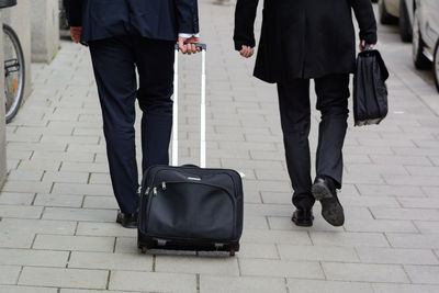 Low section of people with luggage walking on street