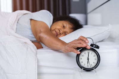 Senior woman pressing alarm clock on bed at home