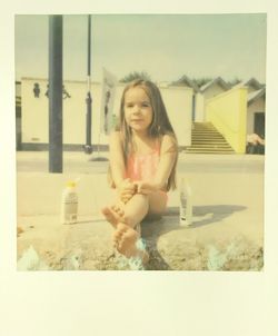 Happy girl sitting on sand at beach against sky