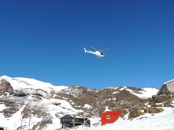 Low angle view of helicopter flying over snowcapped mountain against clear blue sky