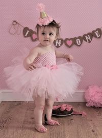 Messy baby girl in dress standing by birthday cake at home