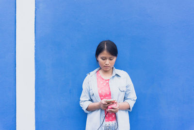 Woman using phone while standing against wall