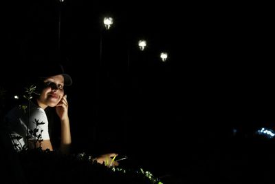 Portrait of woman standing against illuminated lighting equipment at night