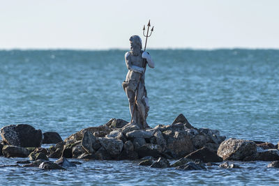 Sculpture on rock by sea against sky