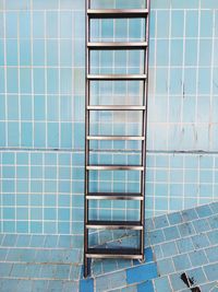 Metallic ladder against blue tile wall in abandoned swimming pool