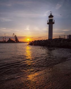 Lighthouse by sea against sky during sunset