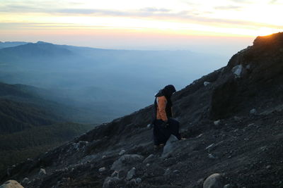 Man standing on rock against sky during sunset