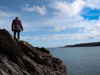 Rear view of man standing on rock by sea against sky