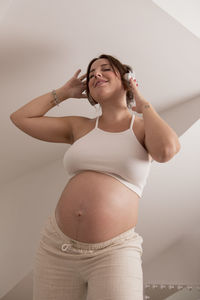 Beautiful pregnant woman, dancing and listening to music on the bed