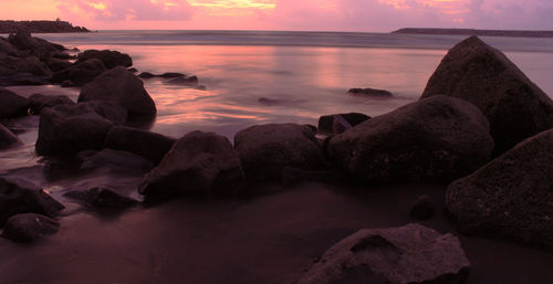 Rocks at sea shore against sky during sunset