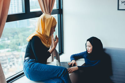 Young woman sitting on window at home