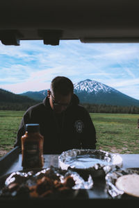 Rear view of man sitting at table against mountains