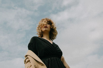 Low angle portrait of woman standing against cloudy sky