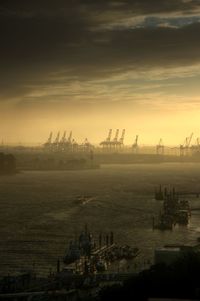 Cranes at harbor against sky during sunset