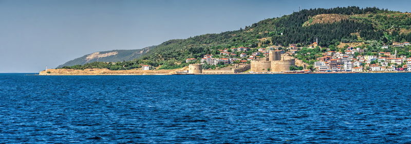 Sea by buildings in town against sky