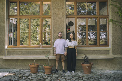 Woman and man standing amidst potted plants in front of window