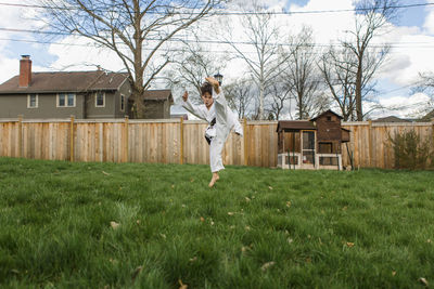 Boy wearing sports uniform kicking in air while practicing karate at backyard