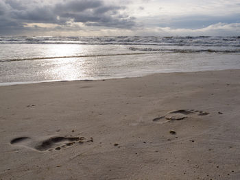 Footprints on sand at beach against sky