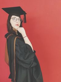 Woman in graduation gown posing by red background
