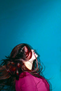 Young woman tossing hair against blue background