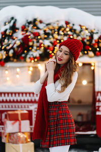 Beautiful young woman with red lips in a warm hat stands by a decorated christmas van on the street