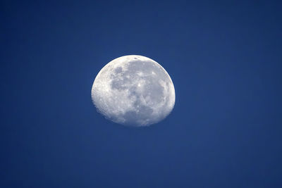 Detail of the moon with visible craters on blue skies. 