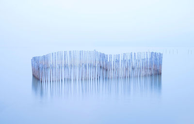 Wooden posts in lake against sky