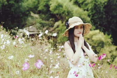 Portrait of young woman wearing hat amidst flowers on field