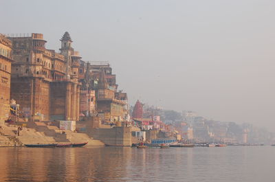 Temples by ganges river against sky during foggy weather