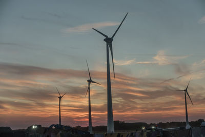 Silhouette wind turbines on landscape against sky at sunset