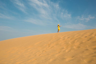 Rear view of woman walking on sand at desert against sky