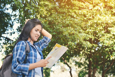 Young woman holding book against trees