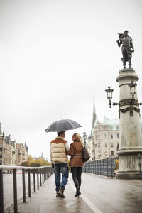 Rear view of young couple with umbrella walking on bridge