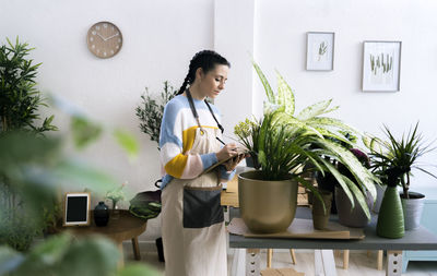Woman standing by potted plant against wall