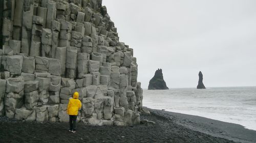 Rear view of man standing on rock by sea against sky