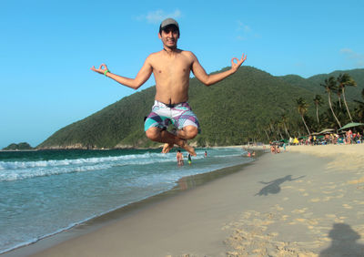 Portrait of shirtless man levitating at beach against sky