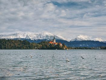 Scenic view of lake bled and snowcapped mountains against sky in autumn.