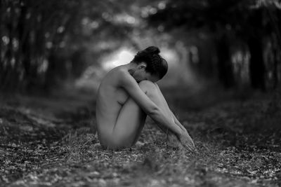 Side view of depressed naked woman sitting on field