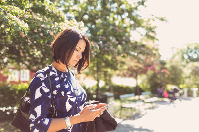 Businesswoman using smart phone on footpath during sunny day