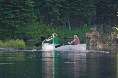 Friends kayaking in river amidst trees in forest