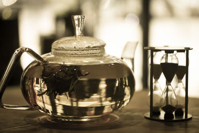 Close-up of herbal tea in pot by hourglass on table