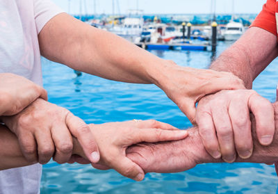 Midsection of senior friends holding hands while standing at harbor