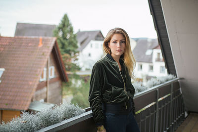 Portrait of woman wearing jacket standing at balcony in town