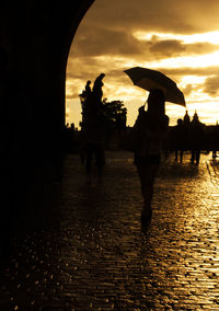 Silhouette people in rain against sky during sunset